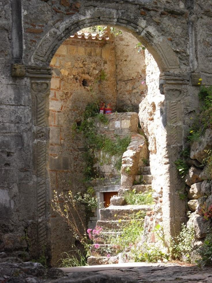 Old stone archway leading to hidden steps among wild plants in Portugal